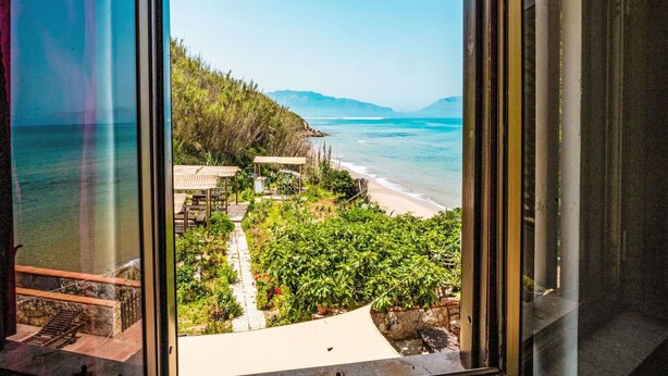 Vista desde una ventana con vista a una playa y un sendero que lleva a una estructura de madera.