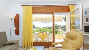 A living room with a sofa, a chair, a glass-top table, and a view of a balcony with outdoor furniture. - Cosy apartment in villa for 5 people with WIFI, TV and terrace (Torroella De Montgrí)
