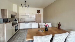 A modern kitchen with white cabinets, a microwave, and a wooden dining table with wicker chairs. - Beautiful apartment for 6 people with WIFI, TV, patio and pets allowed (Zittau)