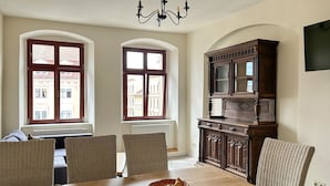 A dining area with a wooden table, wicker chairs, and a dark wooden cabinet with glass doors. - Beautiful apartment for 6 people with WIFI, TV, patio and pets allowed (Zittau)