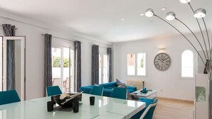 Un salon moderne avec une table à manger en verre, des chaises de couleur turquoise, un canapé et une grande horloge murale.