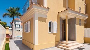 Une maison moderne à deux étages, avec une façade jaune, un balcon et un petit espace piscine.