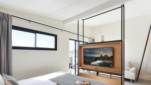 Une chambre d’hôtel moderne avec un grand lit, un téléviseur fixé sur un cadre en bois et une vue sur un paysage montagneux par la fenêtre.