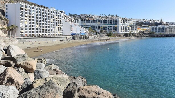 Un hôtel situé sur la côte, avec plusieurs étages, une plage en premier plan et une côte rocheuse.