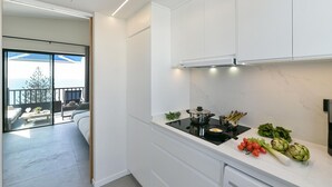 Une cuisine moderne avec des meubles blancs, une plaque de cuisson à induction noire et une vue sur un balcon aménagé avec du mobilier d’extérieur.