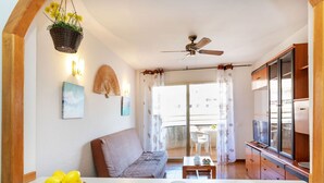 Una sala de estar acogedora con un sofá, una mesa de comedor con dos tazas, un ventilador de techo y una ventana con cortinas.