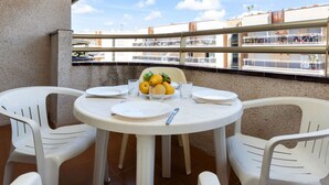 Una mesa redonda con sillas blancas en un balcón, un cuenco de fruta y un vaso de agua.