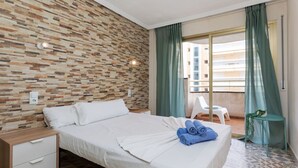 A hotel room with a bed, a nightstand, a small table, a chair, and a balcony with a view. - Beautiful apartment for 4 guests with pool, WIFI, A/C, TV and terrace (Salou)