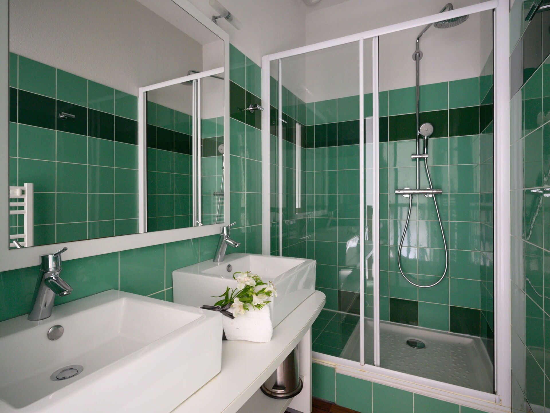 A bathroom with green tiles, a white sink, a mirror, and a shower enclosure.