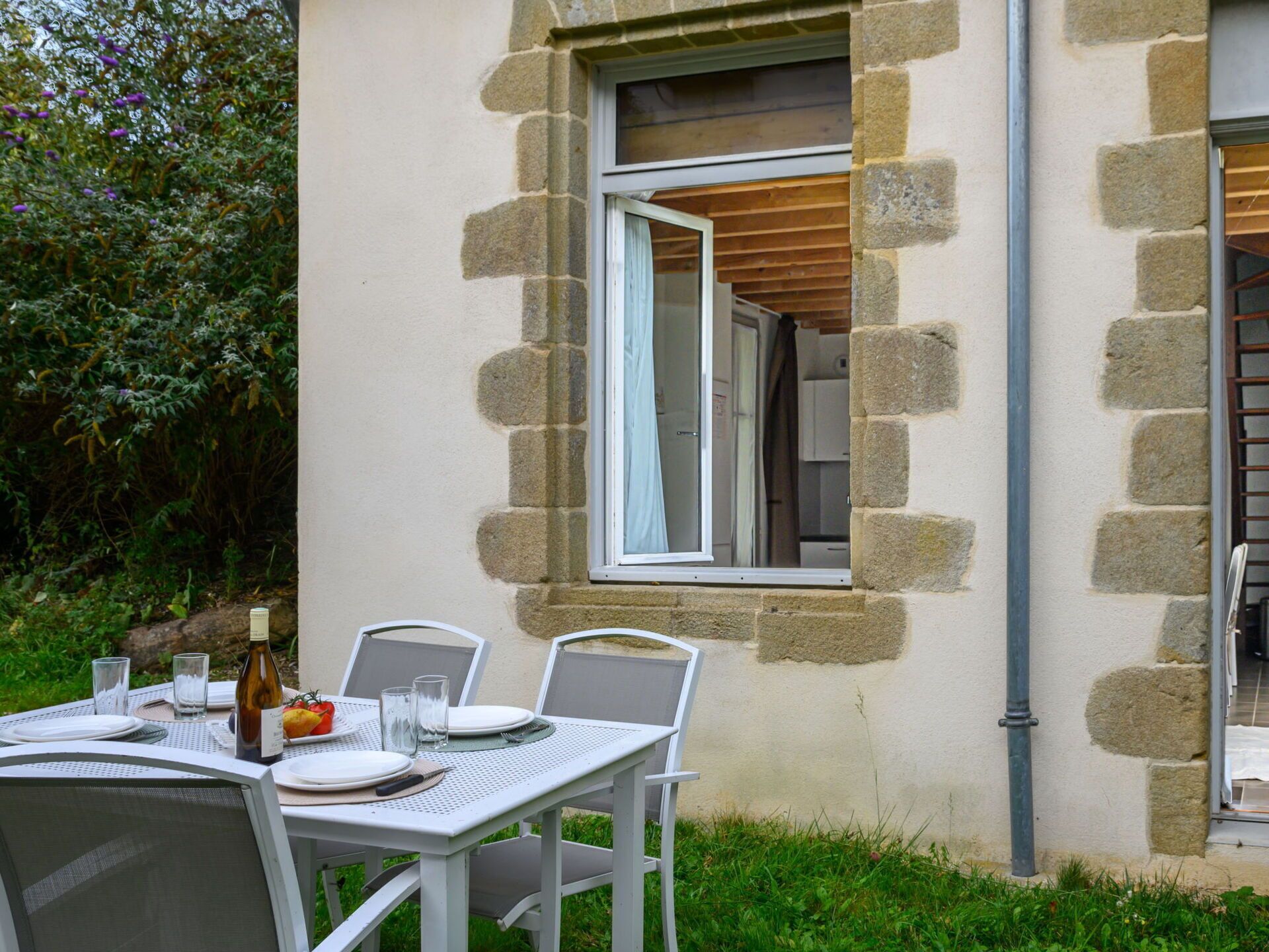 Un área de comedor al aire libre con pared de piedra, una ventana y una mesa preparada para dos.