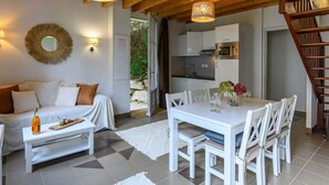 Un salon chaleureux avec un canapé blanc, une table à manger avec des chaises et un coin cuisine équipé d’un four à micro-ondes.