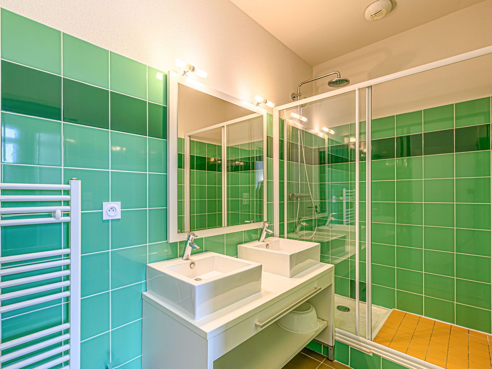 Ein Badezimmer mit grünen Fliesen, einem weißen Waschbecken, einem Spiegel und einer Dusche.