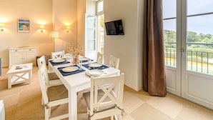 A dining area with a table set for four, a television mounted on the wall, and a view of greenery through the window. - Lovely apartment for 6 guests with pool, WIFI, TV and balcony (Baden)
