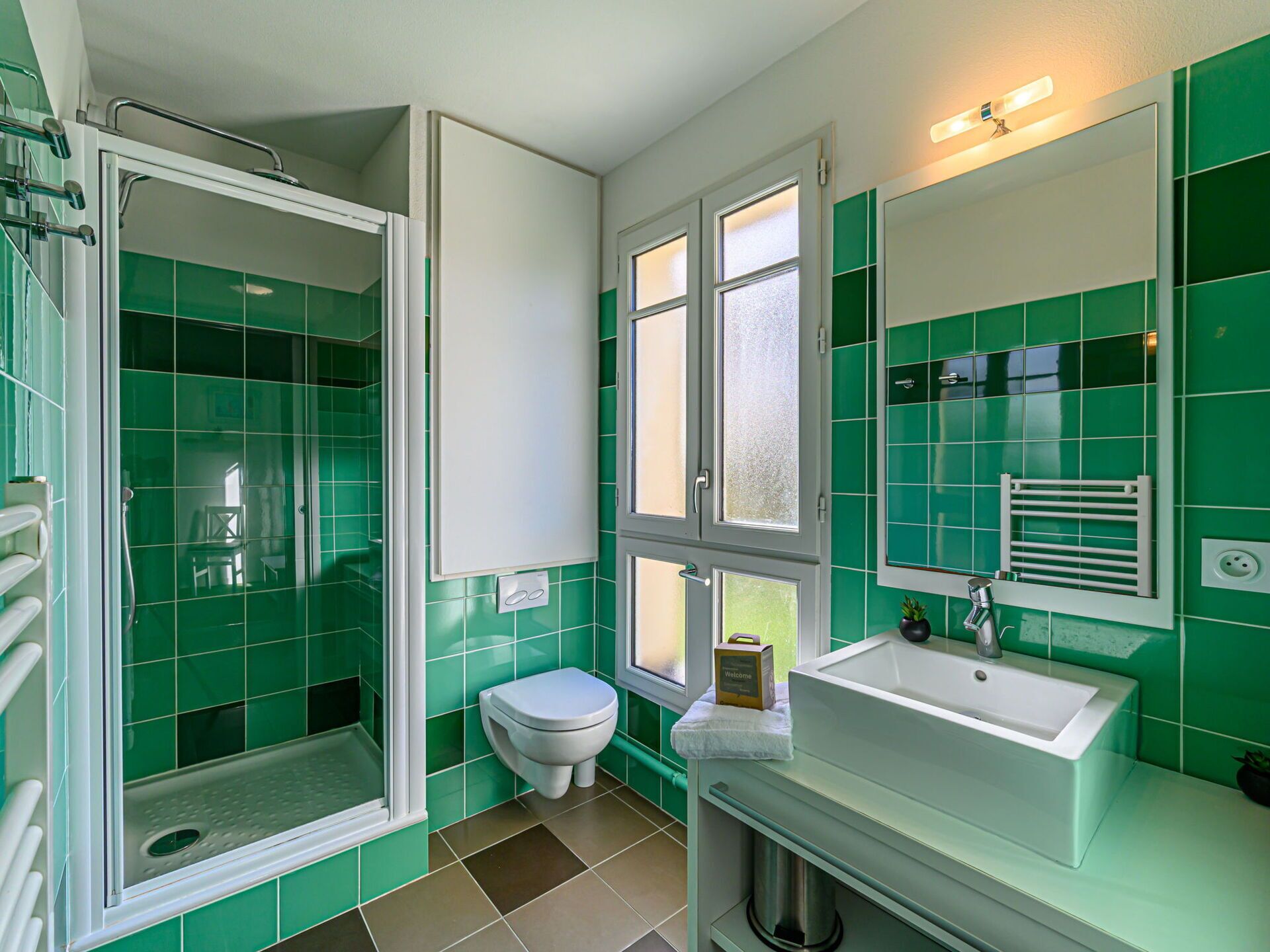 A bathroom with green tiles, a white toilet, a shower with a glass door, and a sink with a mirror.