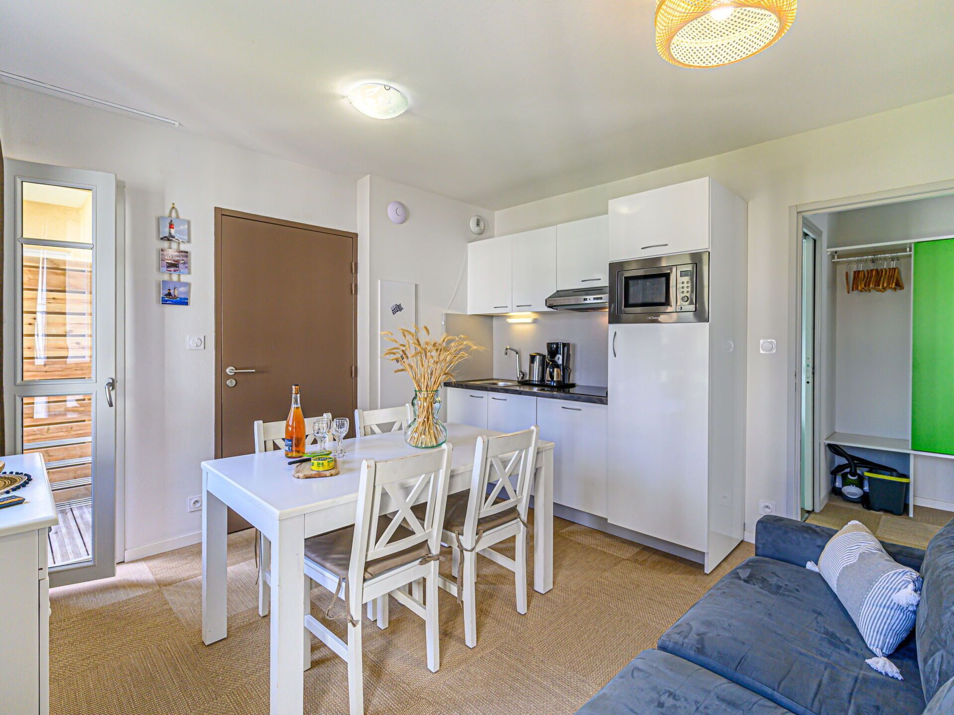 Un espace de vie compact comprenant un coin cuisine, un coin repas avec une table et des chaises blanches, et un canapé gris.