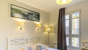 Ett hotellrum med en säng, två vägglampor, en tavla och ett fönster med gardiner.