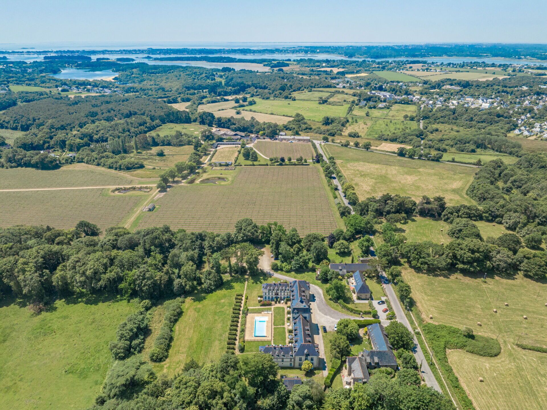 An aerial view of a rural area with a large estate featuring multiple buildings, expansive fields, and a swimming pool.
