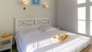 Un lit bien fait, avec du linge de lit blanc, un plateau de petit-déjeuner et deux lampes fixées au mur.