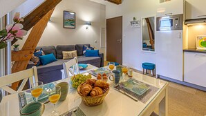Ein gemütliches Wohnzimmer mit einer Couch, einem Esstisch gedeckt mit Frühstück und einer Küche mit Mikrowelle sowie einer Treppe.