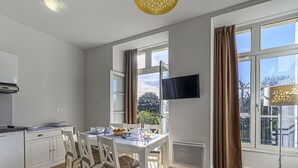 A modern kitchen with white cabinets, a dining table set with chairs, a TV mounted on the wall, and large windows with curtains. - Lovely apartment for 5 guests with WIFI, pool and TV (Baden)