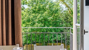 A balcony with a metal railing, a table with a white tablecloth, and a view of a lush green garden. - Lovely apartment for 5 guests with WIFI, pool and TV (Baden)