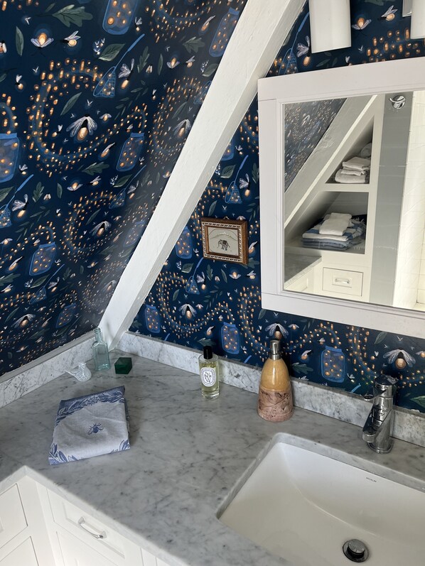 A bathroom with a dark blue patterned wall, a white sink, and a mirror. There are toiletries on the counter, including a bottle of hand soap and a bottle of lotion.