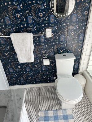 Een badkamer met een donkere, patroonrijke wand, een wit toilet en een klein raam.