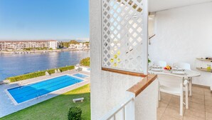 A balcony with a pool, dining area, and view of a river and buildings. - Cosy apartment for 4 people with WIFI, pool, TV, terrace and pets allowed (Empuriabrava)