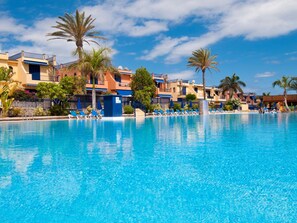 Ein großer Pool mit Liegestühlen und Palmen, umgeben von mehrstöckigen Gebäuden mit Balkonen.