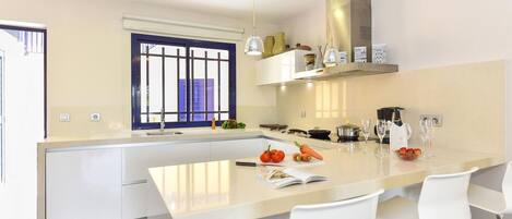 A modern kitchen with a central island, white bar stools, and a window with a blue frame.