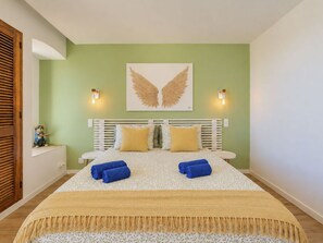 Ein Schlafzimmer mit einem Bett, Kissen, einer Decke, einer Wandleuchte und einem dekorativen Wandbild.