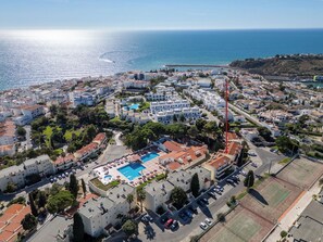 An aerial view of a coastal town with a prominent swimming pool complex surrounded by residential buildings.