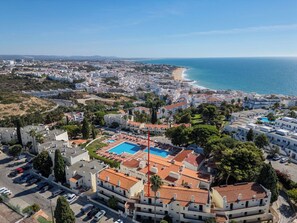 Zona residencial costeira com um grande complexo de piscinas, rodeada por edifícios brancos e telhados em tijolo vermelho.