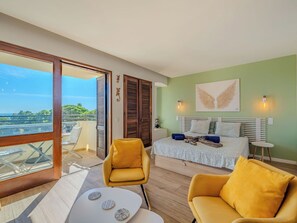 A bedroom with a bed, two chairs, a table, and a balcony with a view.