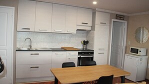 A compact kitchen with white cabinets, a wooden table, and a microwave. - Douarnenez, Proche de la Plage des Sables Blancs à Tréboul (Douarnenez)