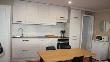 A compact kitchen with white cabinets, a wooden table, and a microwave.