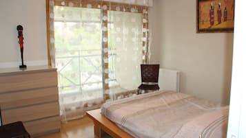 A bedroom with a bed, a wooden bench, a radiator, and a window with curtains.
