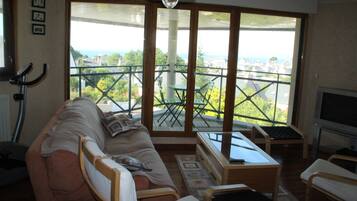 Un soggiorno con divano, tavolo e televisore. Un balcone offre vista sulla città.