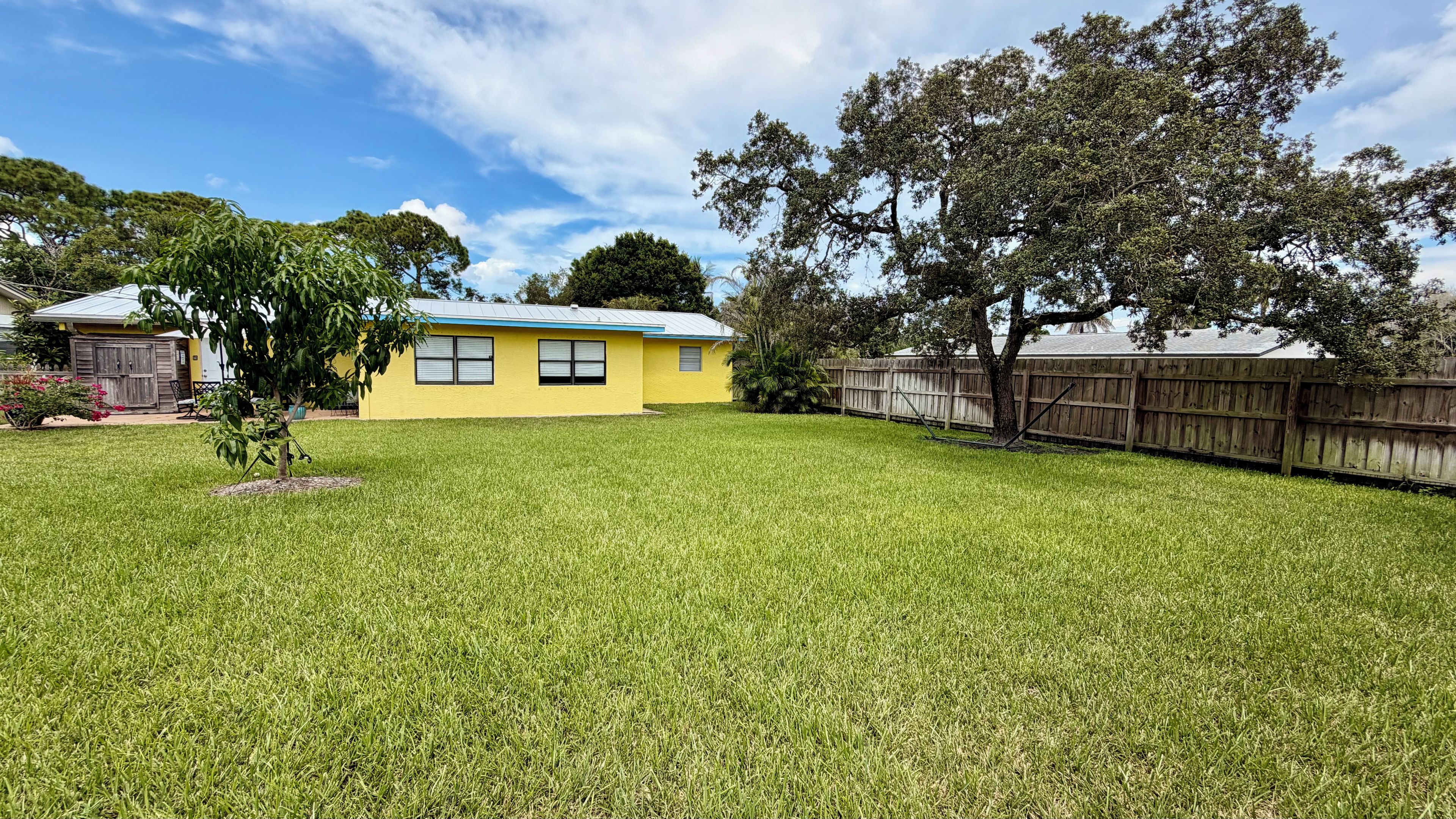 A residential property with a well-maintained lawn, a yellow house with a blue roof, and a wooden fence.
