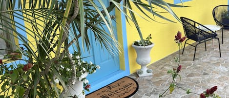 A yellow building with a blue door, a stone patio, and a welcome mat.