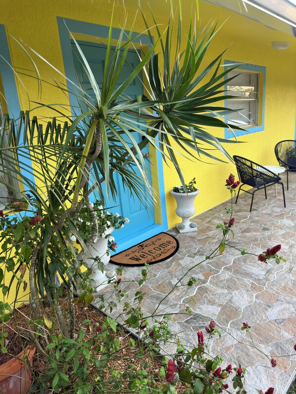 A yellow building with a blue door, a stone patio, and a welcome mat.