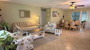 A living room with a sofa, armchair, coffee table, and dining area with chairs and a table. - Casa Celeste. Fenced Back Yard. Close to Boat Ramp. Children and Dog Friendly.   (Palm City)