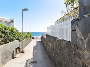 A narrow stone pathway leading to a beach, flanked by white fences and greenery.