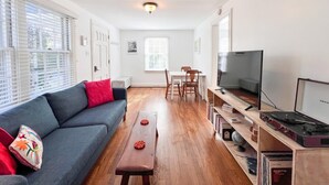 A modern living room with a sofa, a coffee table, a TV, and a bookshelf. - Updated 1BR cottage on private acre+ lot (Winston-Salem)