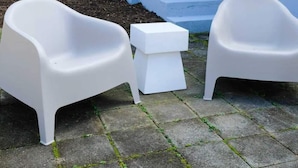 Two white plastic chairs and a small white table on a paved surface. - Updated 1BR cottage on private acre+ lot (Winston-Salem)
