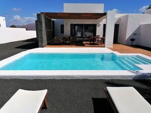 A modern outdoor pool area with a clear blue pool, two lounge chairs, and a patio with outdoor furniture. - Beautiful apartment in villa for 4 guests with WIFI, A/C, private pool, TV and terrace (Playa Blanca)