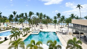A resort with a large swimming pool, beachside lounge areas, and palm trees.