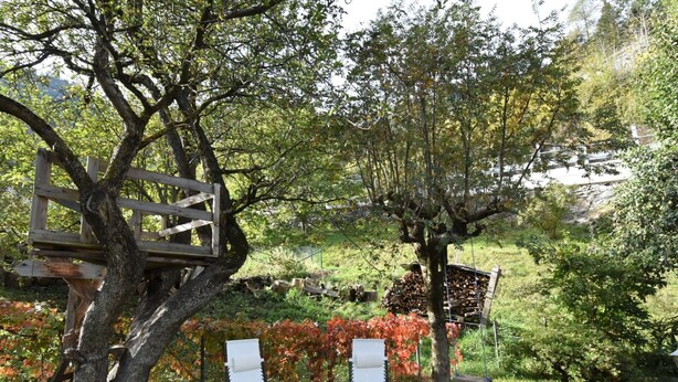 Ein Garten mit zwei weißen Liegestühlen, einer Holzterrasse und einer Schaukel.