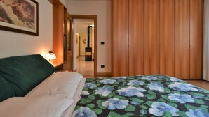 Ein Schlafzimmer mit einem Bett, einem Holzschrank, einem Nachttisch mit Lampe und einem gerahmten Bild an der Wand.
