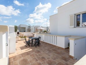 Eine Dachterrasse mit Tisch und Stühlen, einem Grill und Blick auf die umliegenden Gebäude.